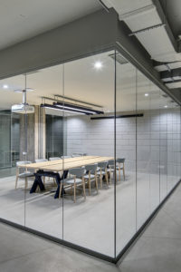 Glowing office in loft style Luminous conference zone in the office in a loft style with brick walls and concrete columns. Zone has a large wooden table with gray chairs and glass walls. Above the table there is a projector.